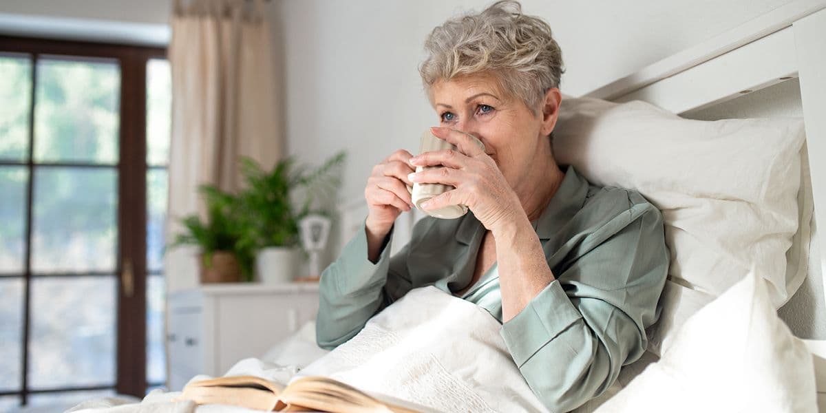Senior woman in bed drinking from mug