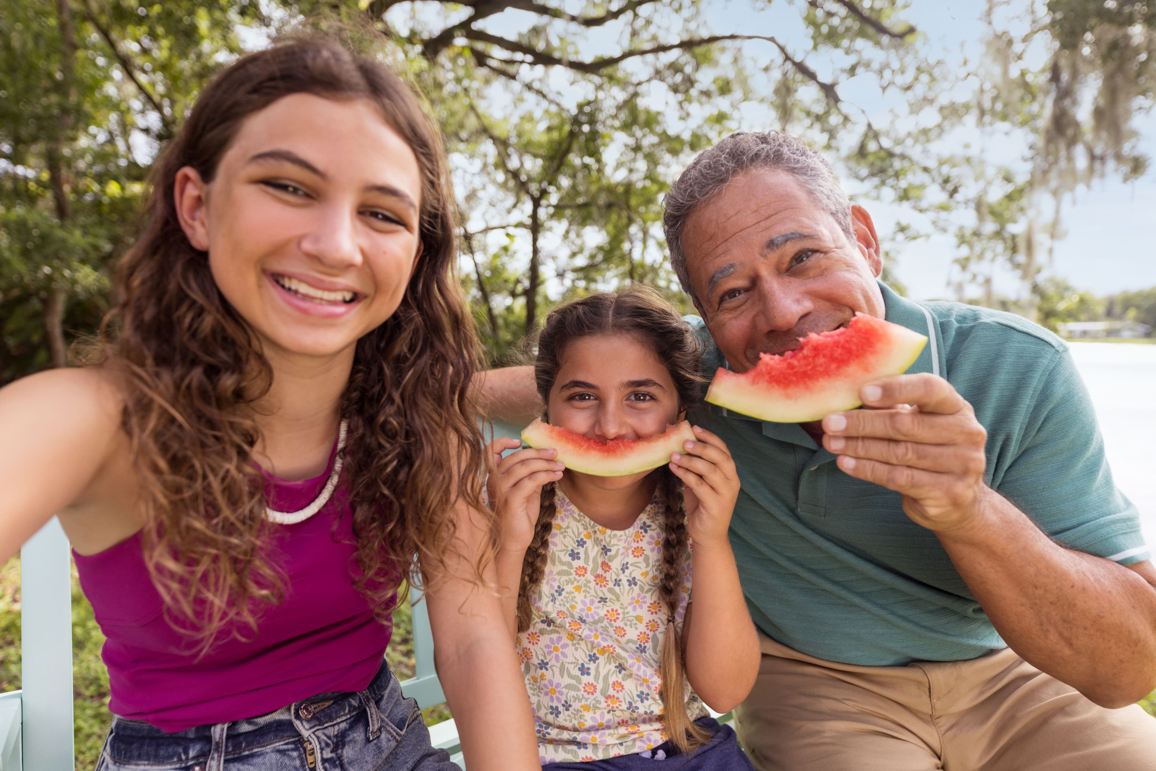 Hispanic grandfather with grandchildren outside eating watermelon