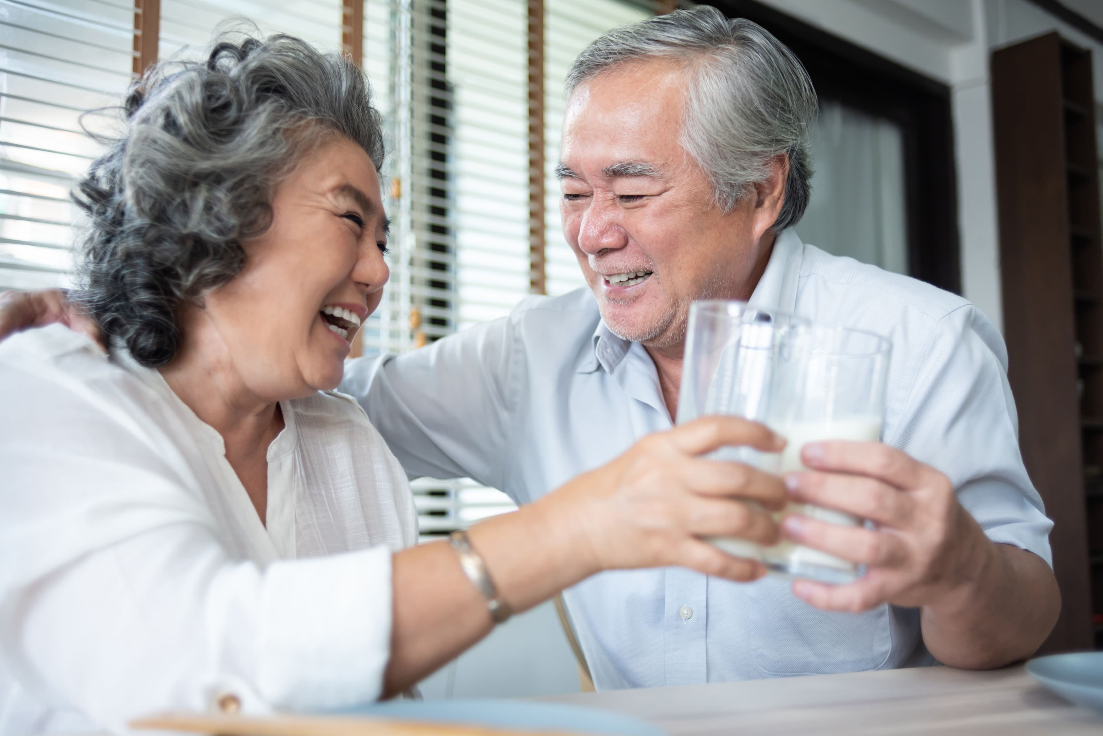 Happy Asian Senior Couple laughing and drinking milk from the glasses together on the morning.