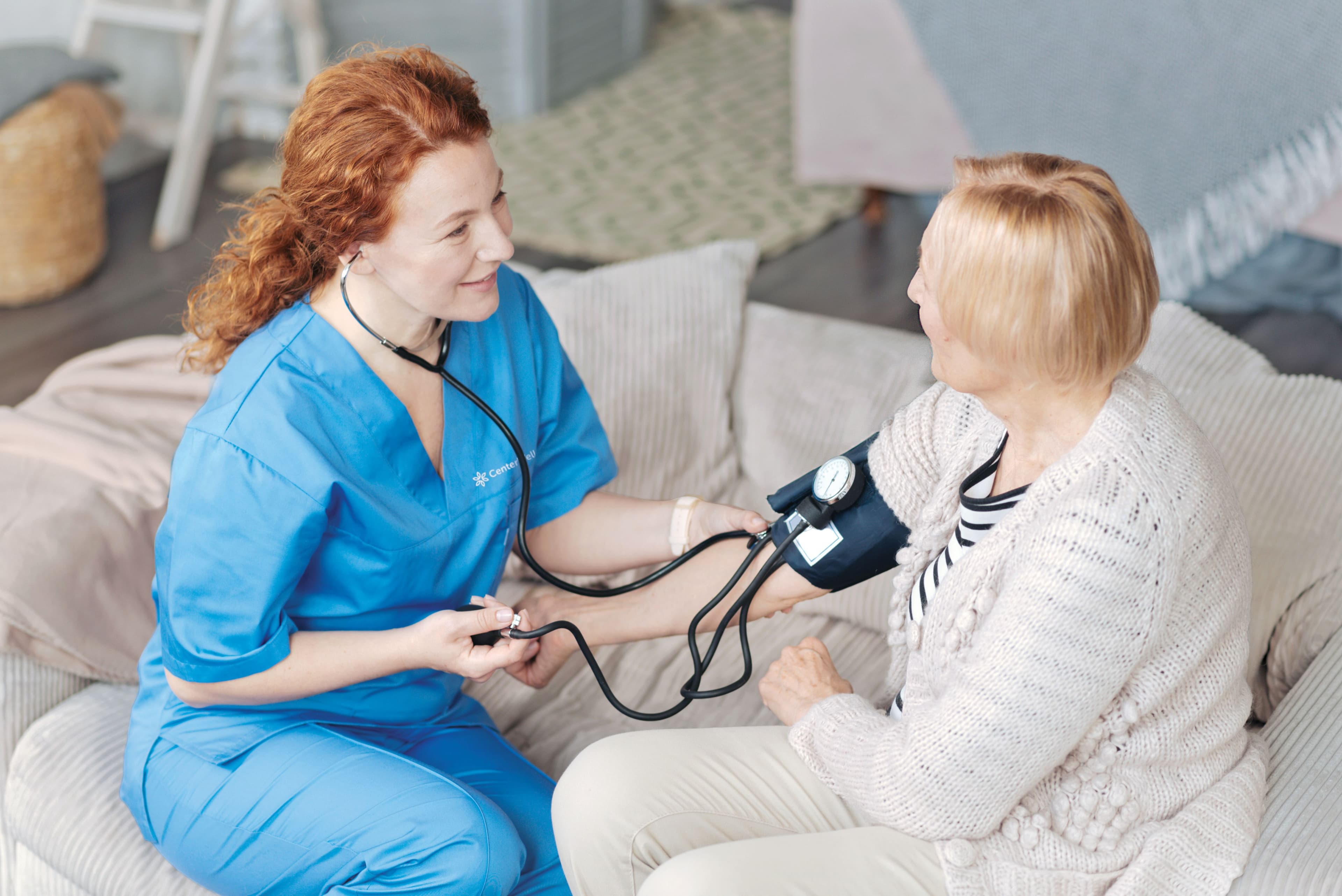 Nurse assists elderly woman on measuring blod pressure in a living room
