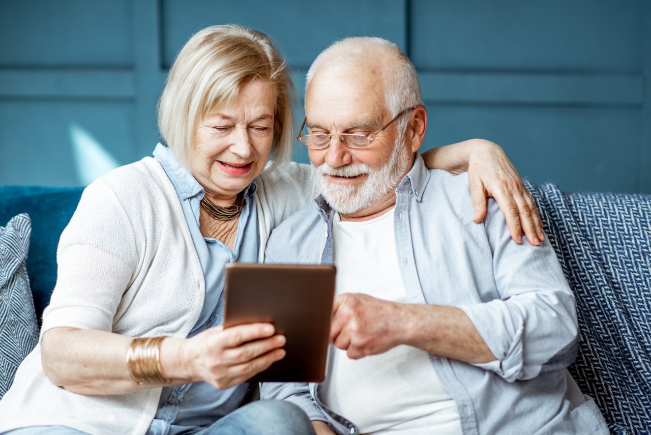 Senior couple dressed casually using digital tablet while sitting together on comfortable couch at home